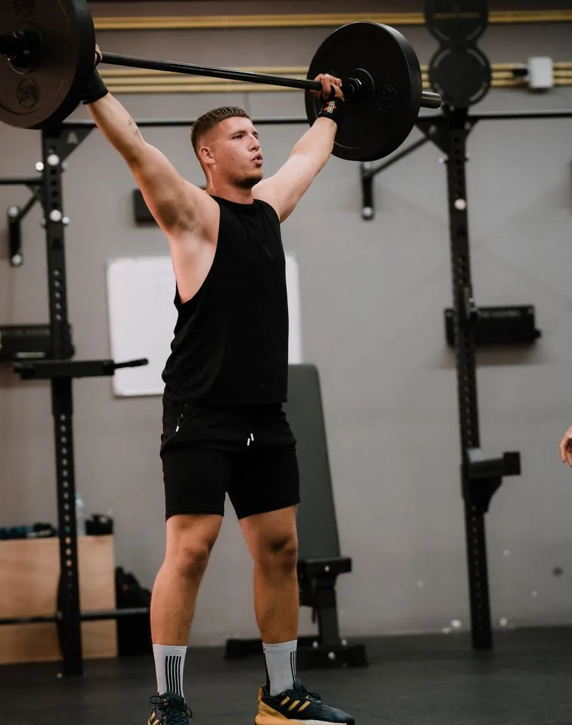 An athlete pressing a loaded barbell overhead with focused intensity during a coached session