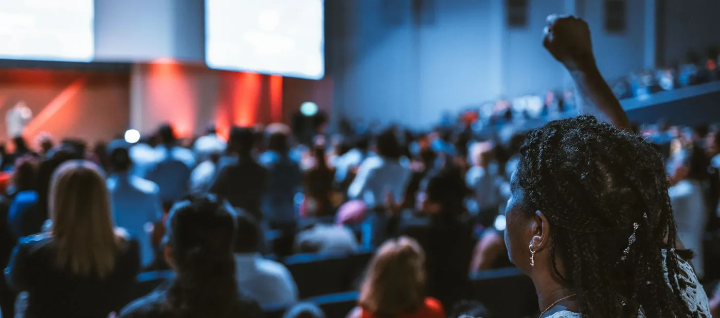 Rising Voices — a neighbor raising a fist in a packed community meeting