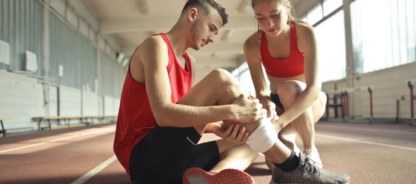 Apex Performance Lab — coach steadying an athlete recovering from a knee injury on the track